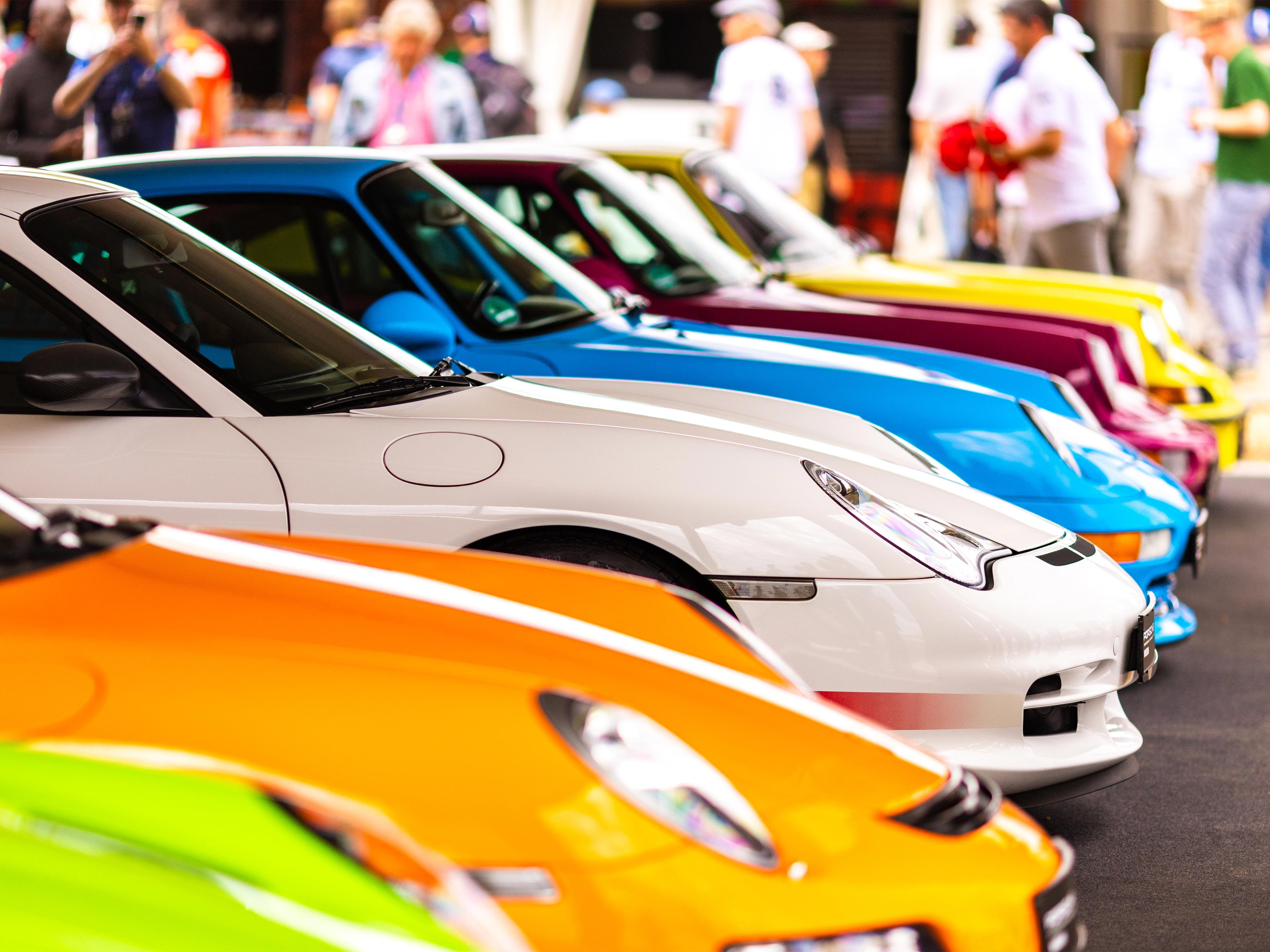 Mehrere bunte Porsche Sportwagen parken in einer Reihe.