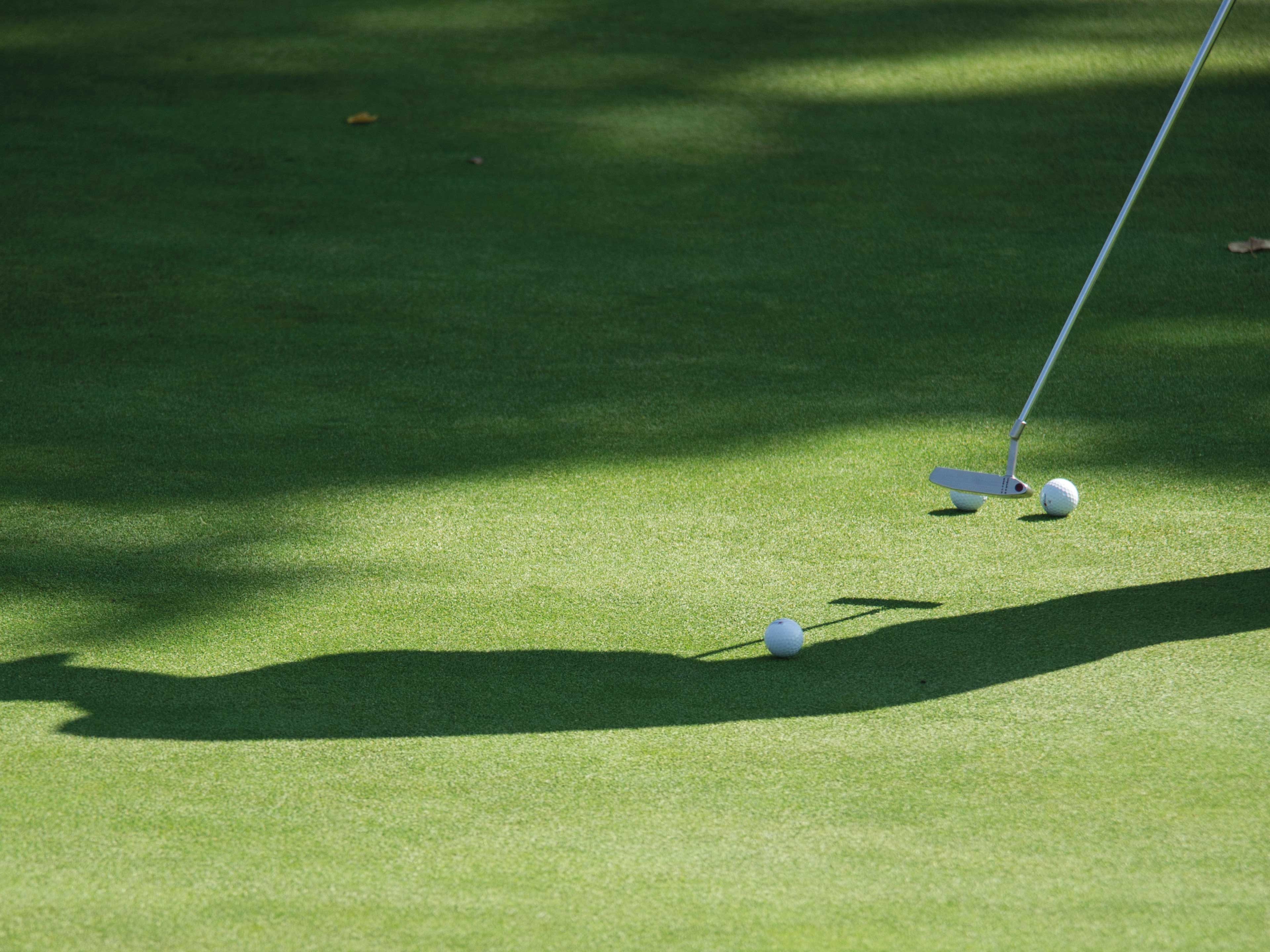 Eine Detailaufnahme von einem Golfschläger mit drei Golfbällen auf dem Rasen.