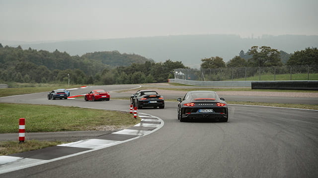 Mehrere Porsche Sportwagen fahren auf einer Rennstrecke.